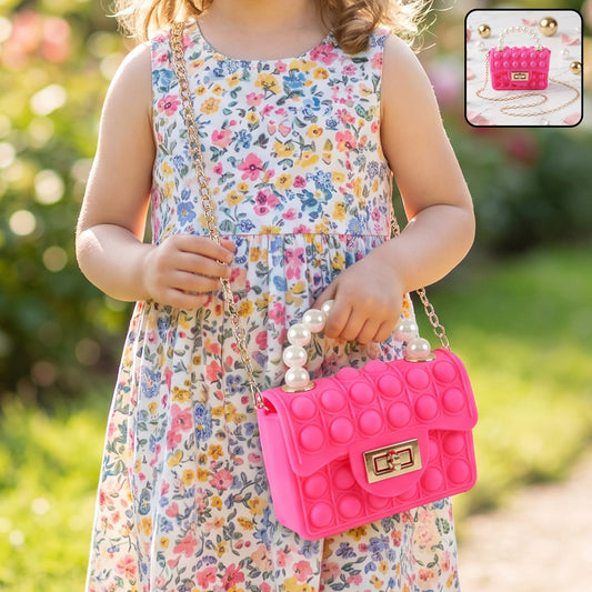 A young girl in a floral dress holds a bright pink pop-it purse with a pearl handle and gold chain.
