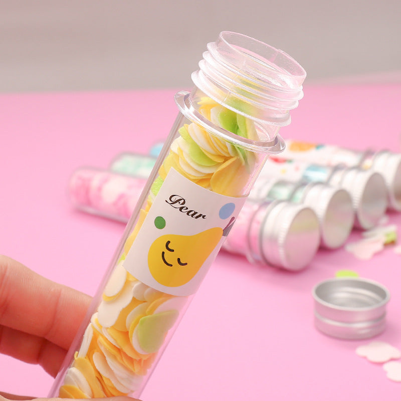 A hand holds an open clear tube of yellow and green flower-shaped paper soap strips with a pear label on a pink background.