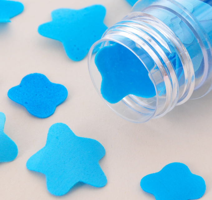 A clear tube lies on its side, spilling out blue flower-shaped paper soap strips onto a light surface.