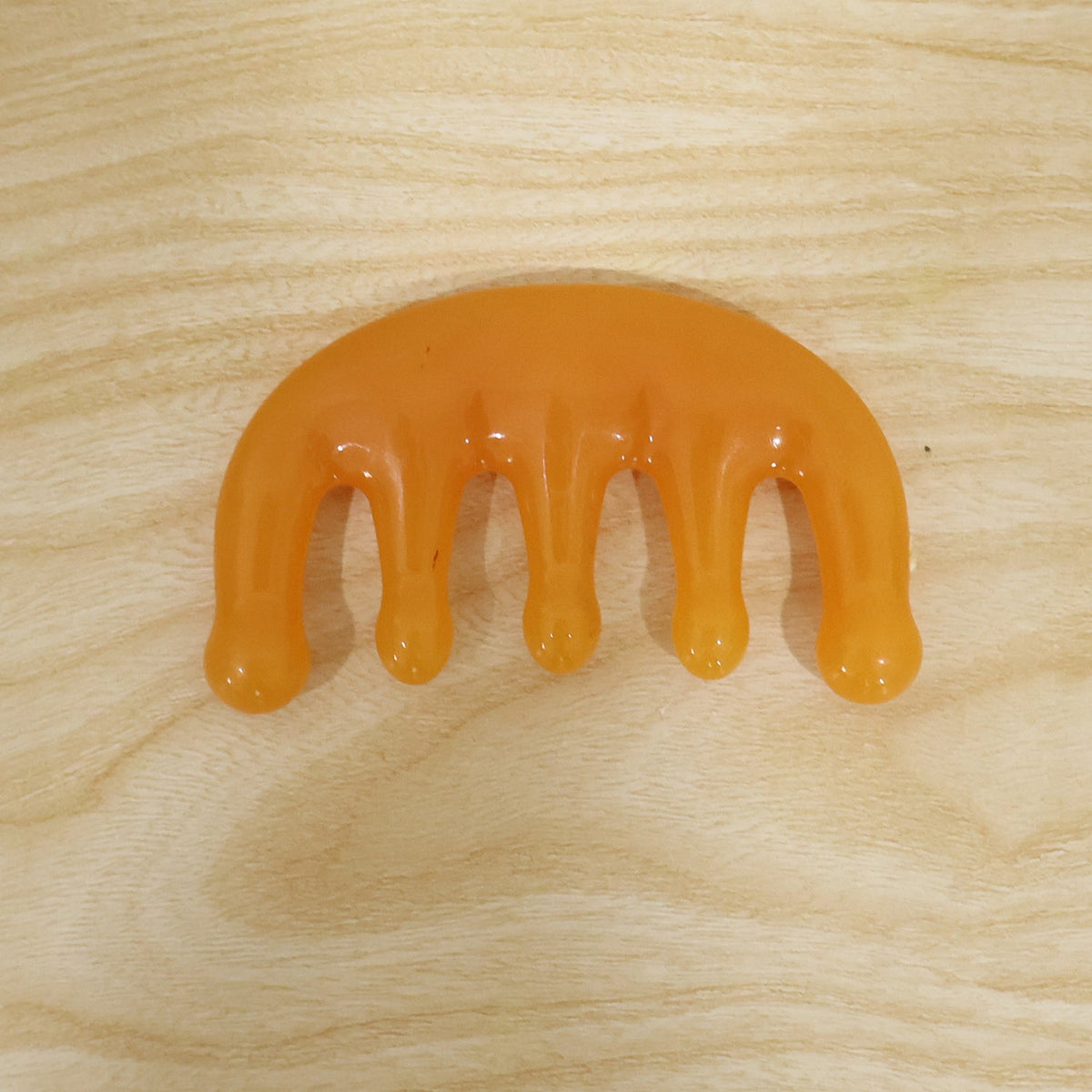 The orange scalp massager comb lies flat on a light-colored wooden background with visible grain.