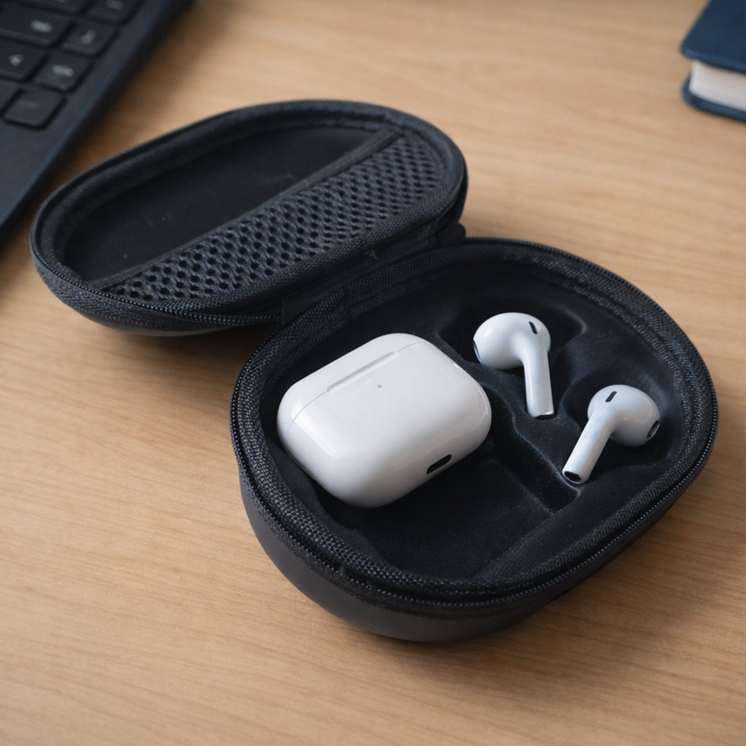 An open black hard shell case on a wooden desk contains white earbuds and their charging case in molded compartments.