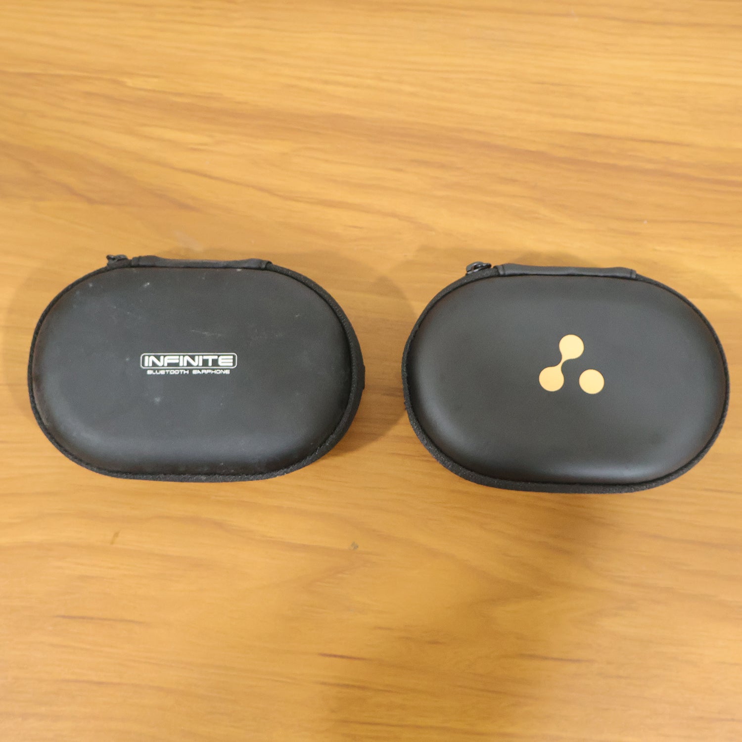 Two closed black hard shell cases are side-by-side on a wooden surface, one with a logo, the other with text.