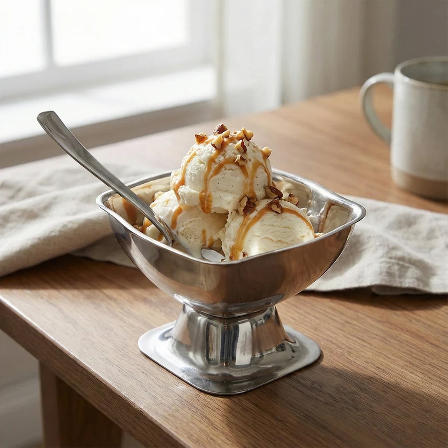A single stainless steel ice cream cup filled with vanilla ice cream, caramel, and nuts, with a spoon.