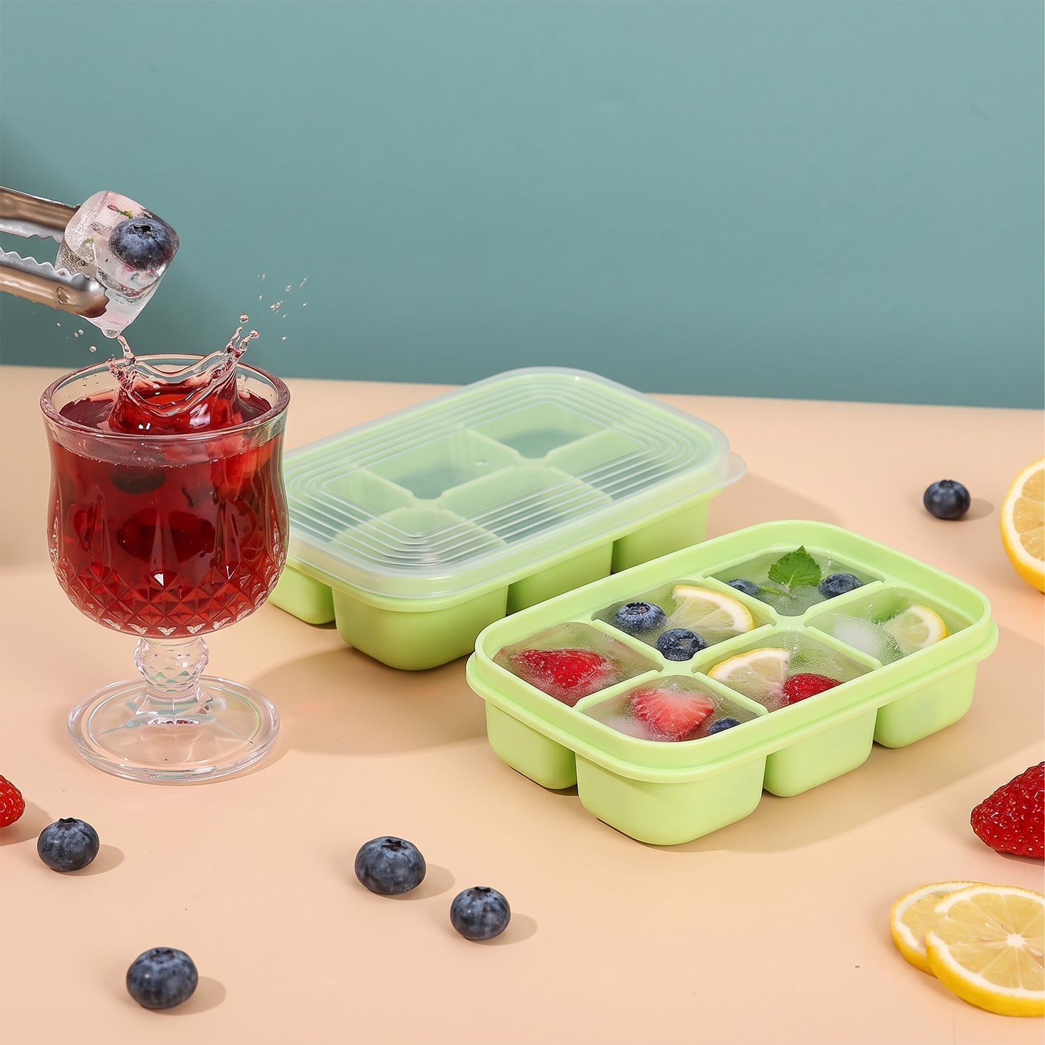 Two green 6-cavity ice cube trays, one with a clear lid, next to a glass of red drink with an ice cube being dropped in,