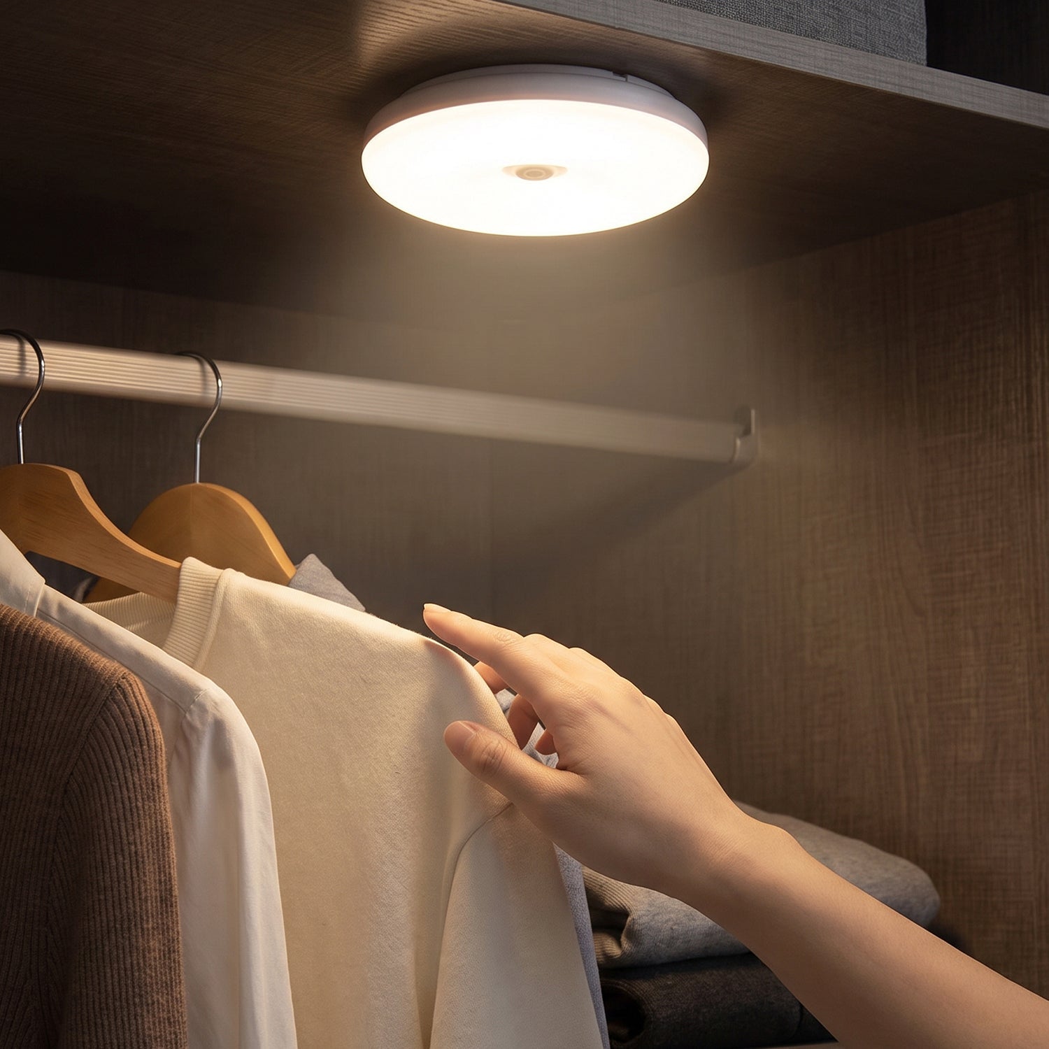 A hand selects clothing from a closet, illuminated by a bright, round LED light mounted on the top shelf