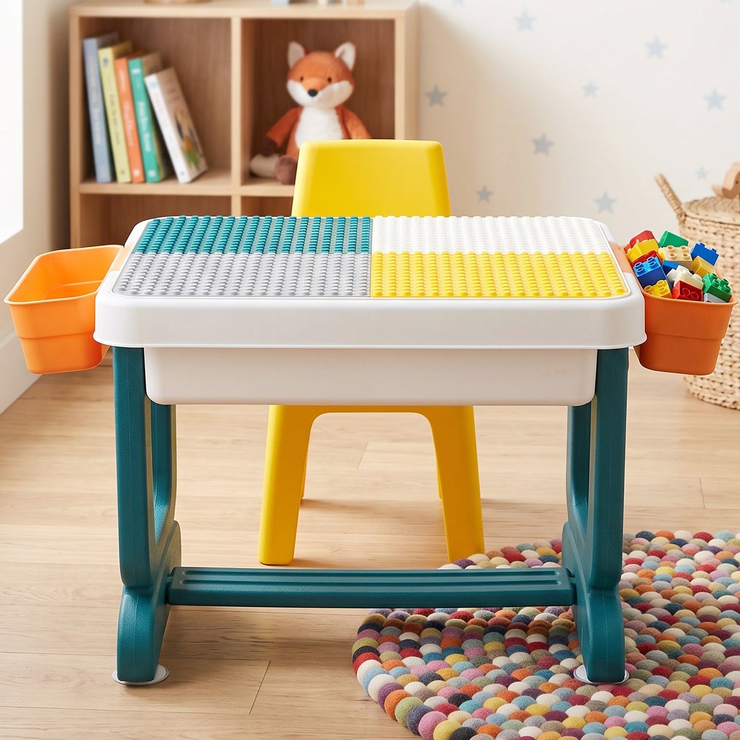 A teal and white activity table with a four-color building block surface and two orange storage bins.