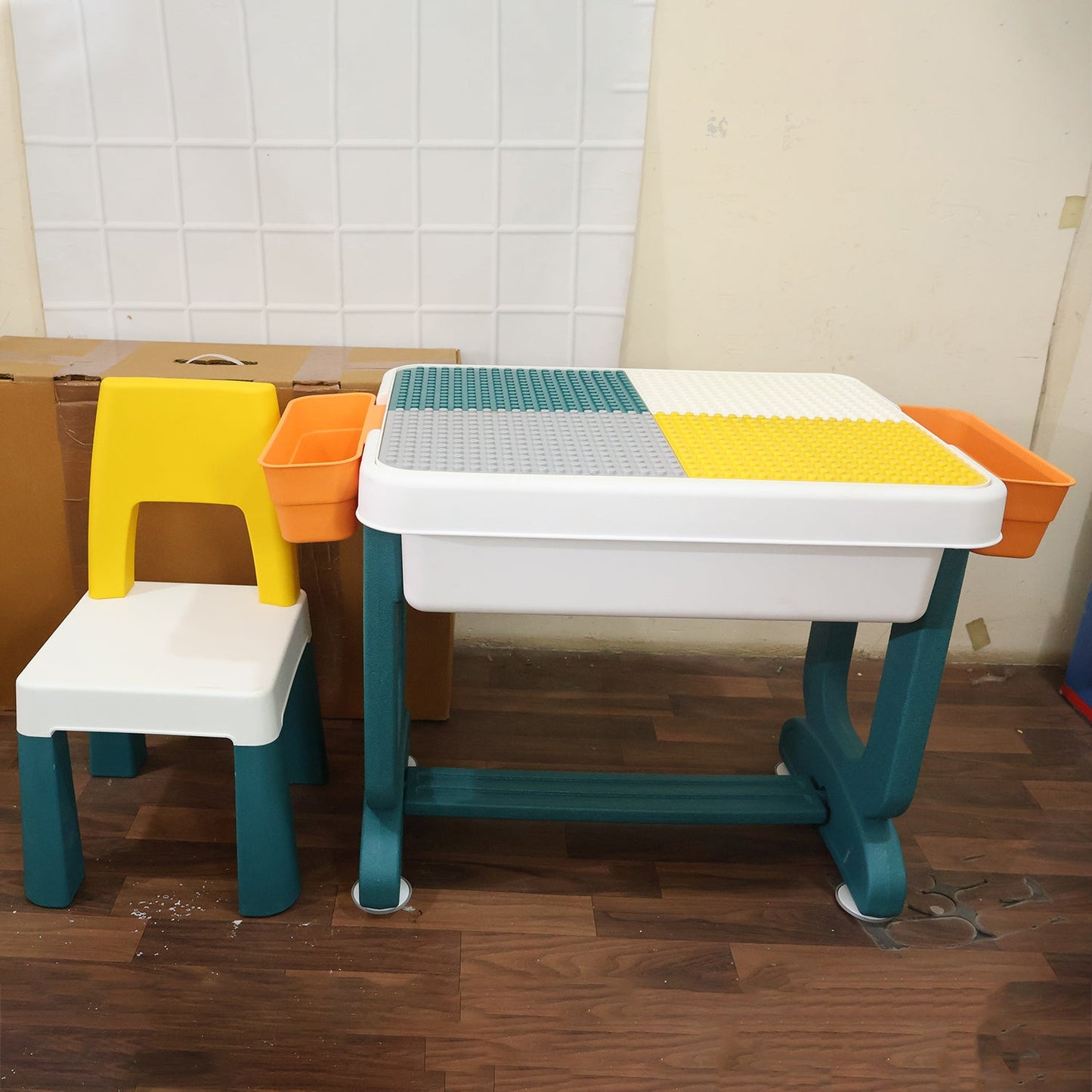 A yellow and white plastic chair sits next to a teal and white activity table with a four-color building block surface and