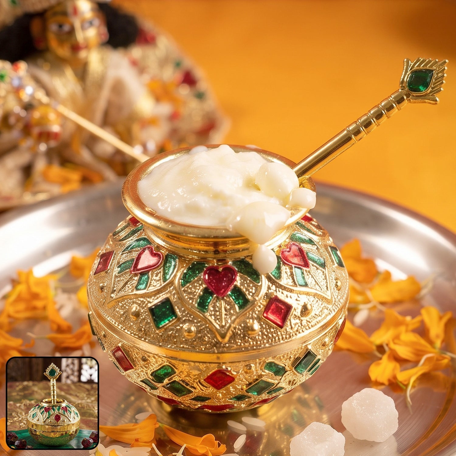 A gold decorative pot with a matching spoon, both adorned with red and green enamel, hold white butter on a silver tray.