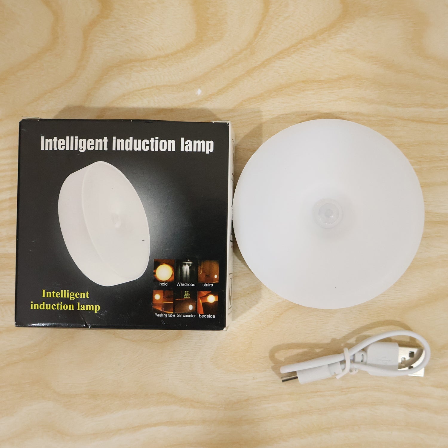 A white circular LED light, its USB cable, and a black box labeled