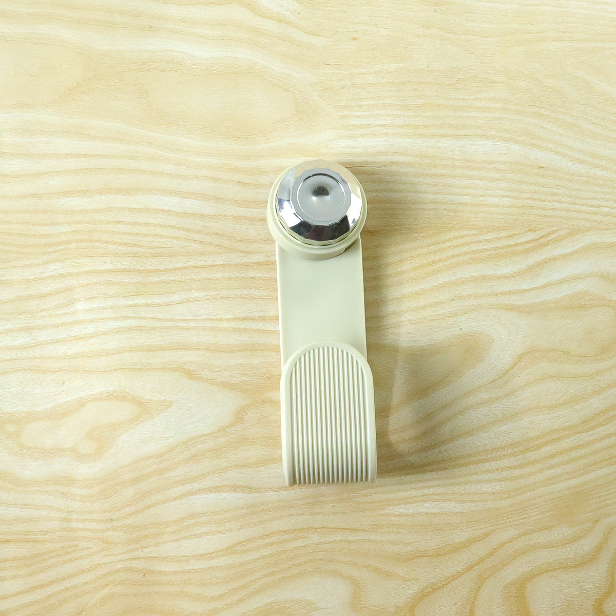 A cream-colored hook with a chrome top and ribbed texture is presented on a light wood grain surface.