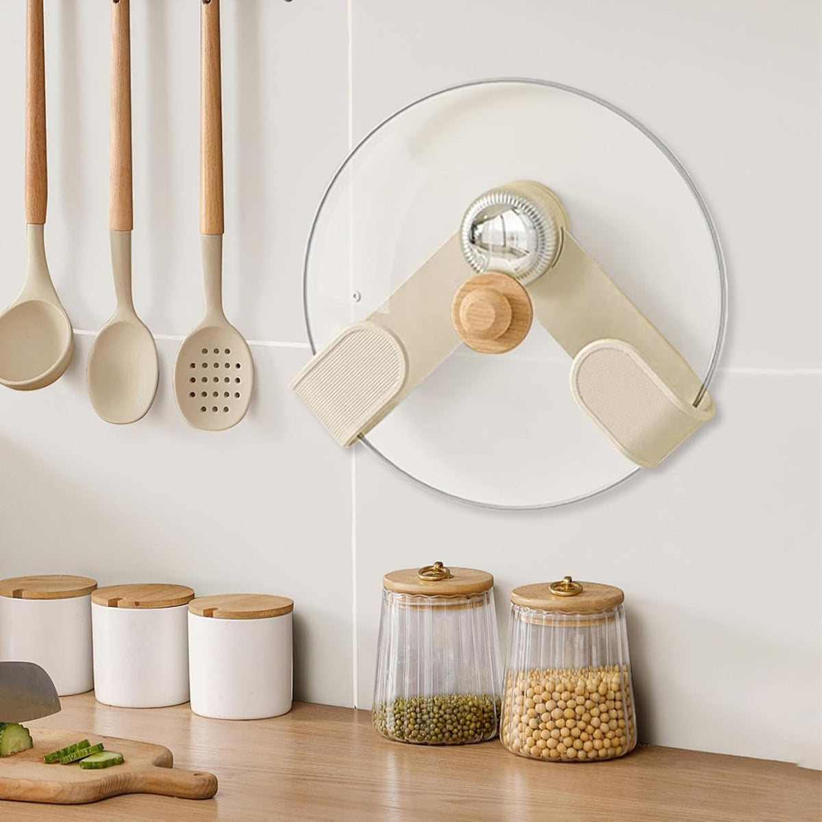A cream pot lid holder with a wooden knob and chrome center holds a glass lid on a white tiled wall above kitchen counter