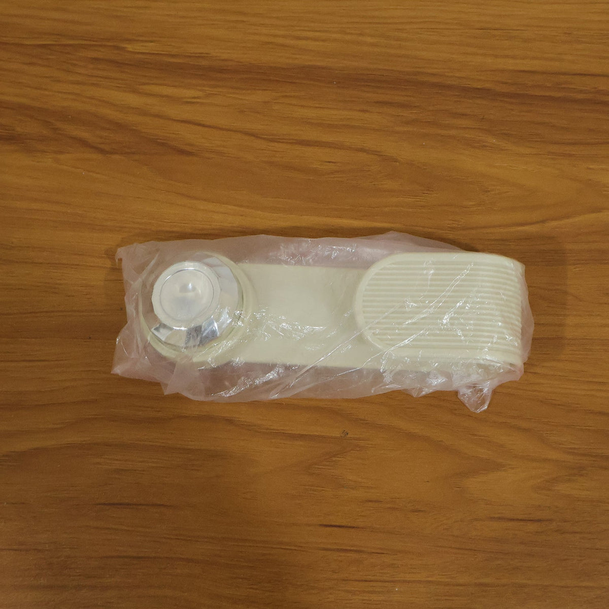 A cream-colored pot lid holder, folded into a straight shape, is sealed in clear plastic packaging on a wooden surface.