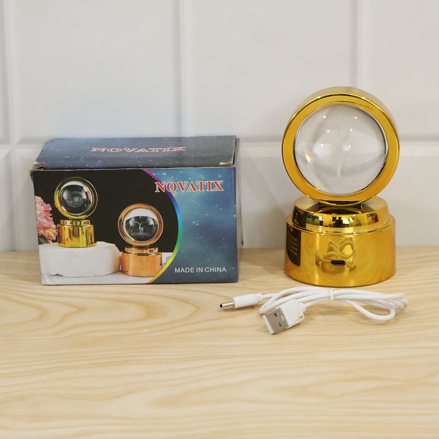 A golden 3D Crystal Ball LED Table Showpiece with a white opaque ball, a white charging cable, and a blue product box.