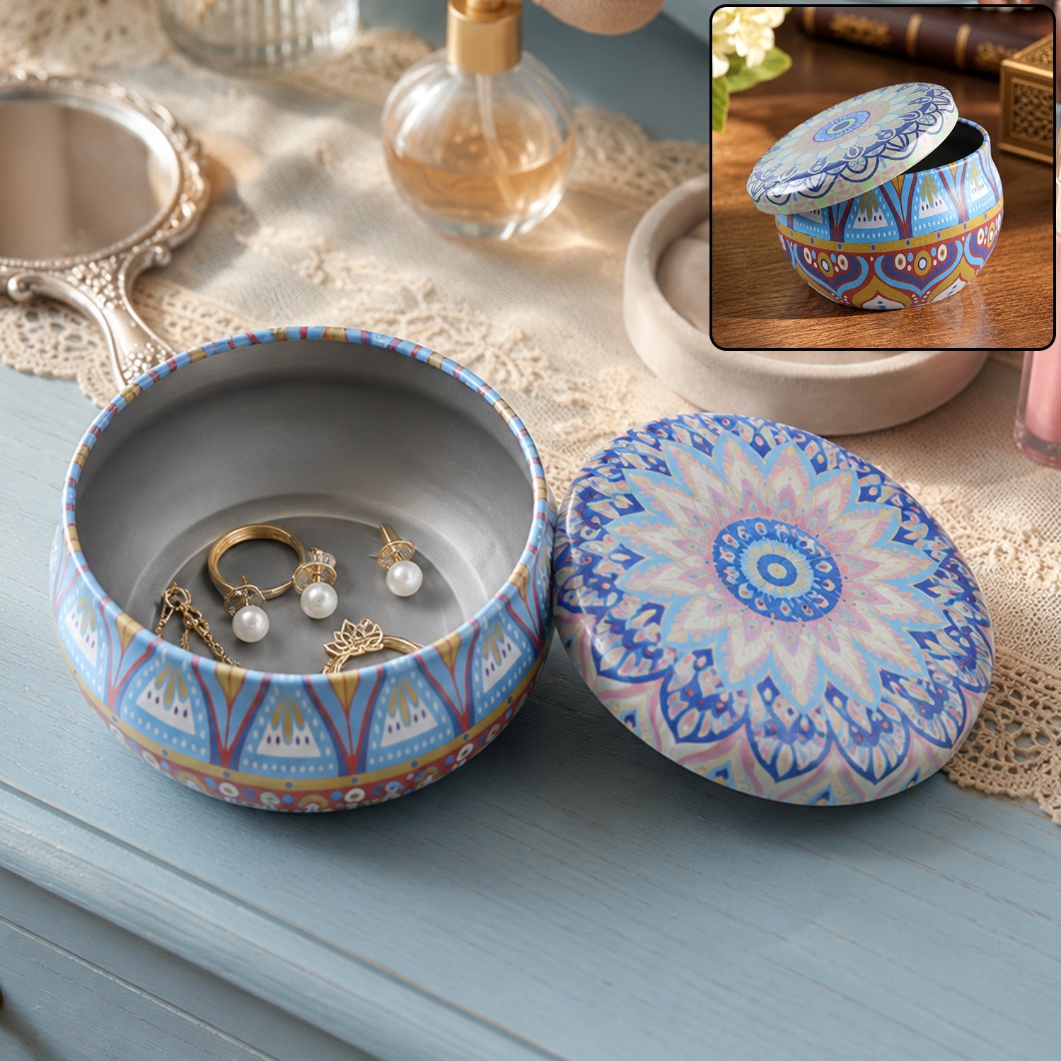 An open blue and orange mandala tin box with a lid next to it, holding gold rings and pearl earrings.