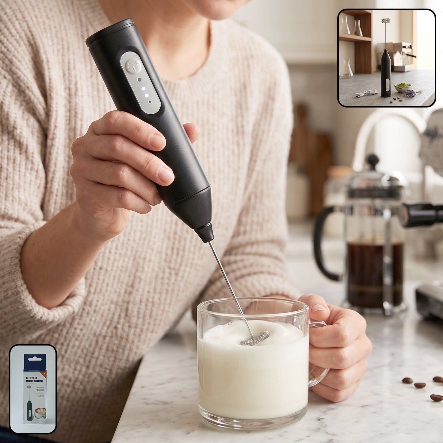 A person in a beige sweater holds a black electric milk frother, whisking milk in a clear glass mug on a marble counter.