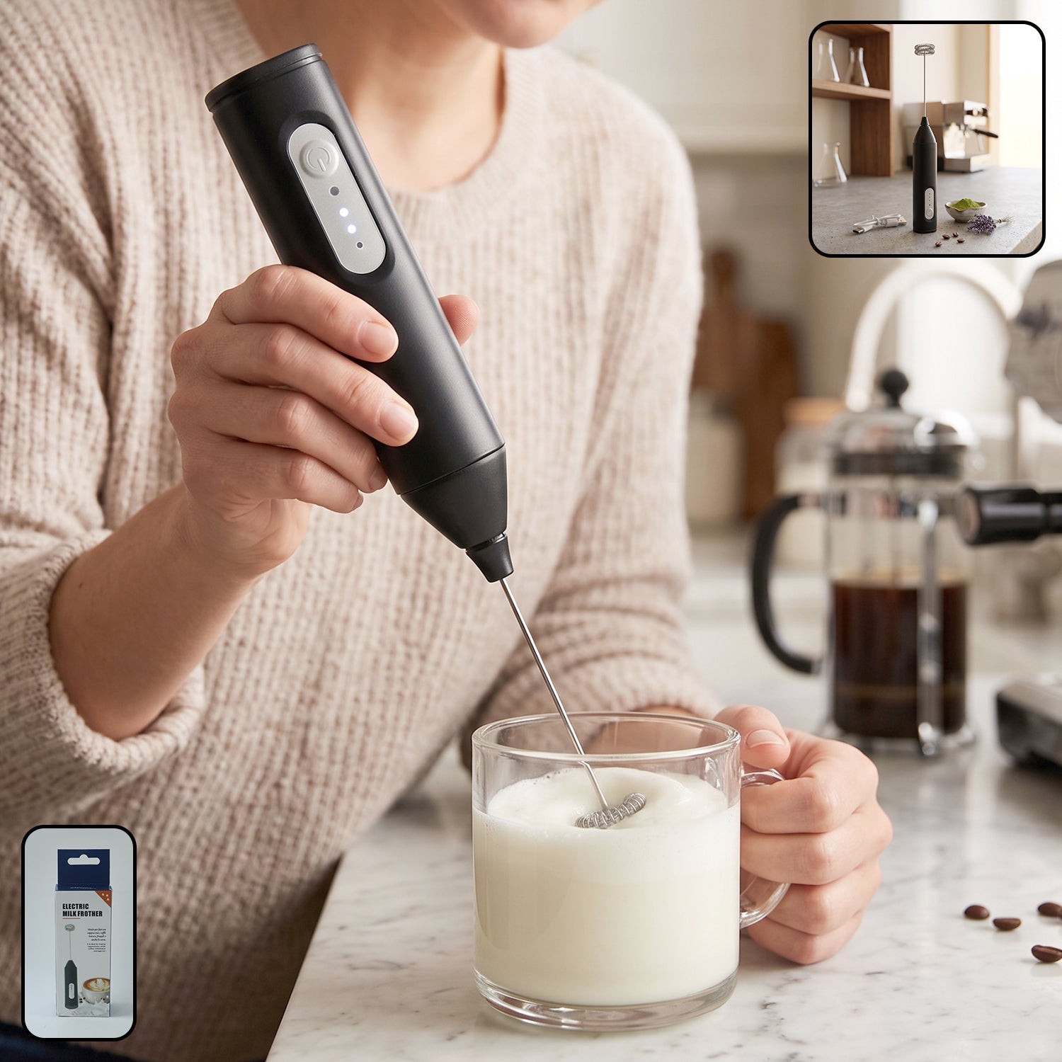 A person in a beige sweater holds a black electric milk frother, whisking milk in a clear glass mug on a marble counter.