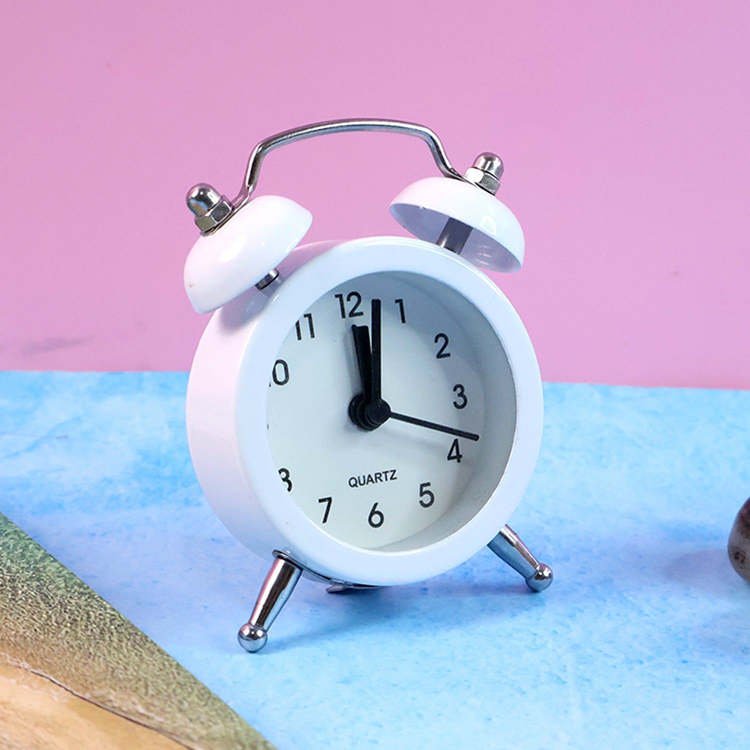Small twin-bell analog alarm clock featuring sturdy metal legs.