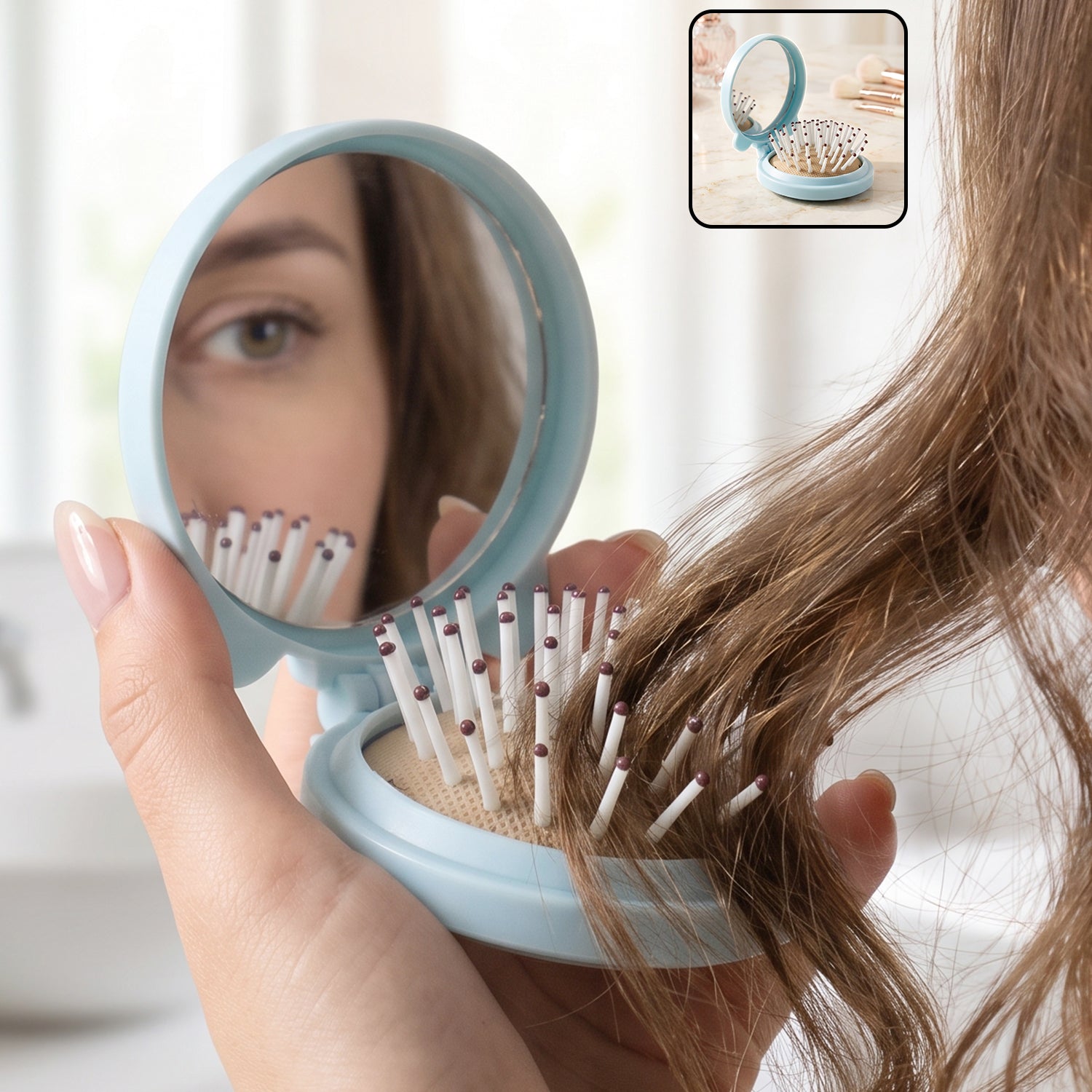 A woman's hand holds a light blue folding hairbrush with a mirror, reflecting her eye and the brush bristles.