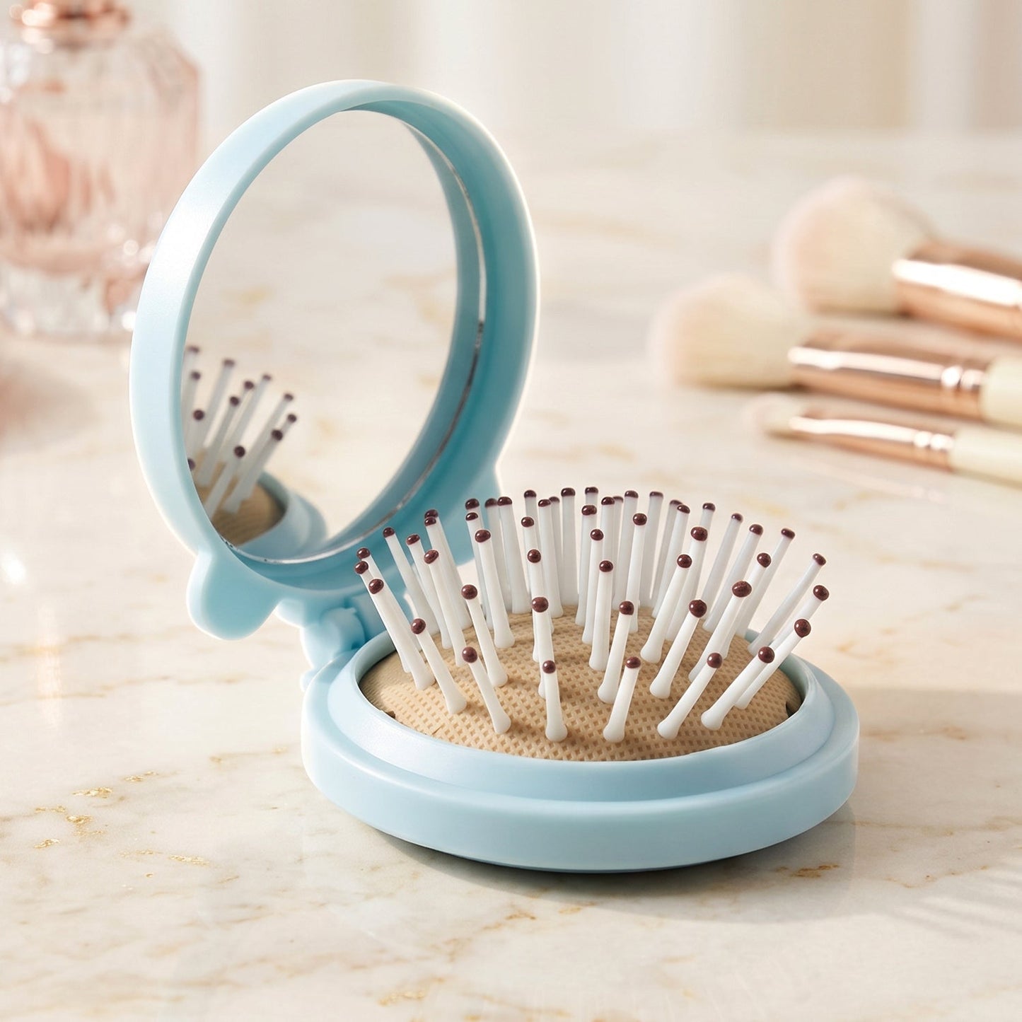 A light blue folding hairbrush with a mirror stands open on a marble surface, with makeup brushes in the soft background.