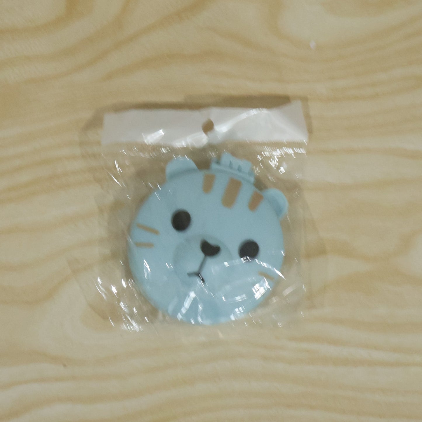 A light blue folding hairbrush with a cartoon bear face is sealed in clear plastic packaging on a light wooden surface.