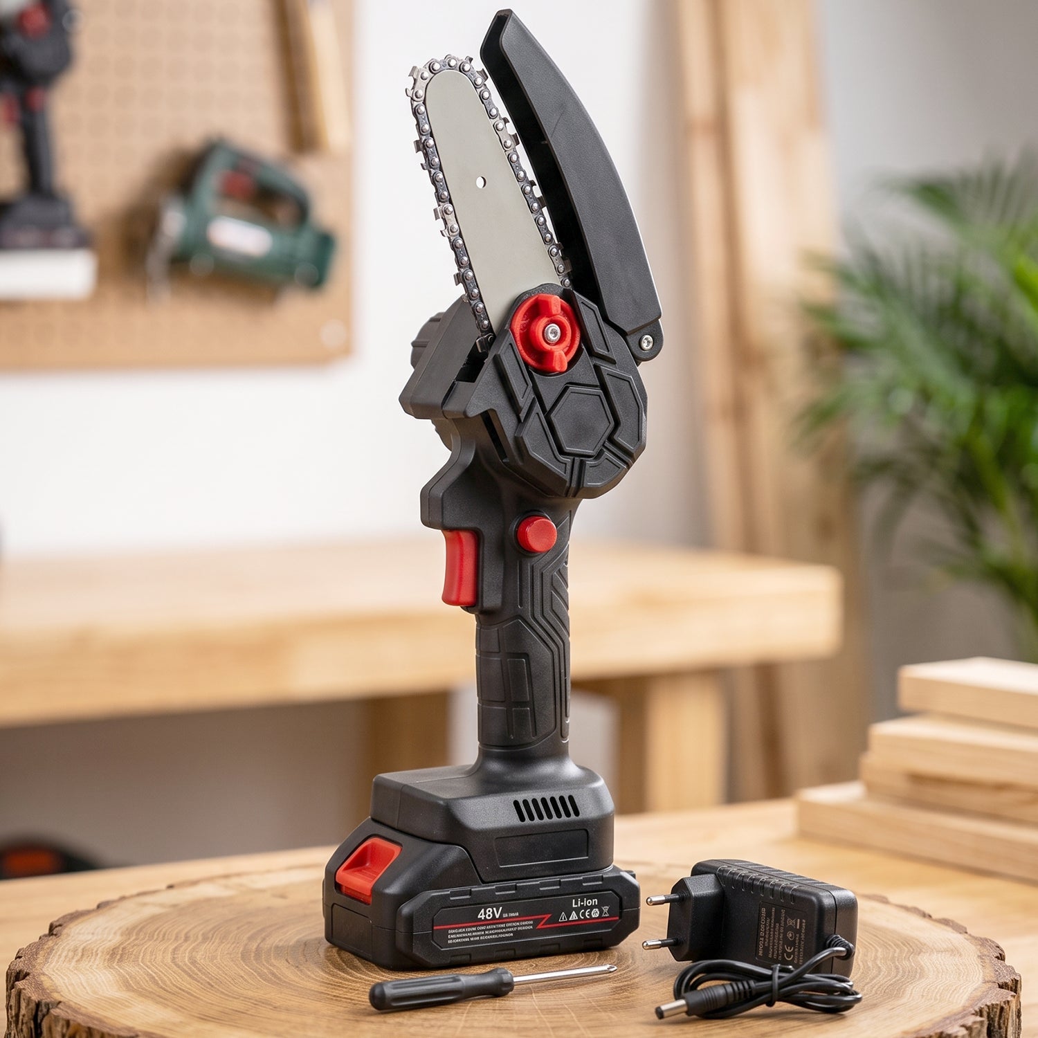 Gloved hand holding a black and red mini chainsaw, cutting a tree branch in a sunny garden.