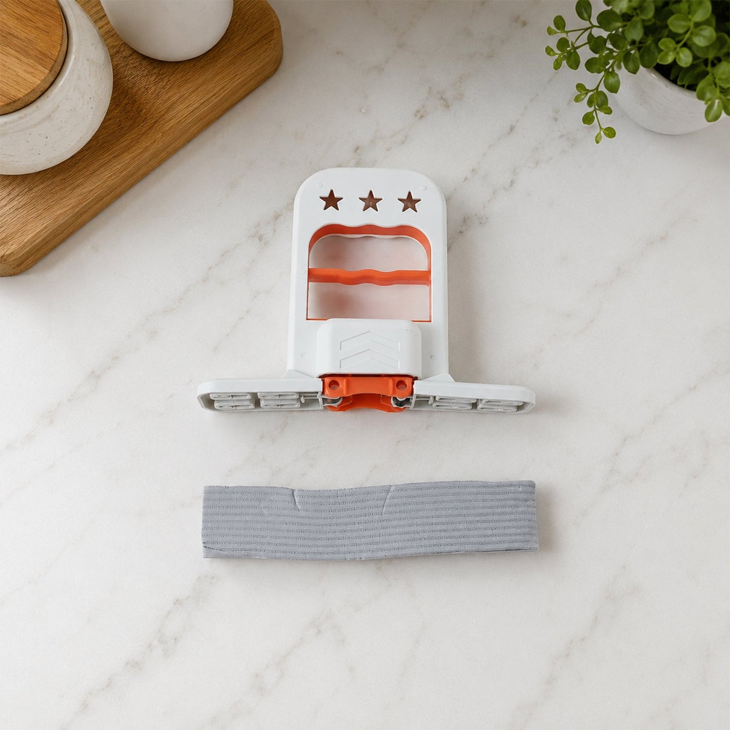 The white and orange mini mop is disassembled on a white marble countertop, with the gray sponge separate.