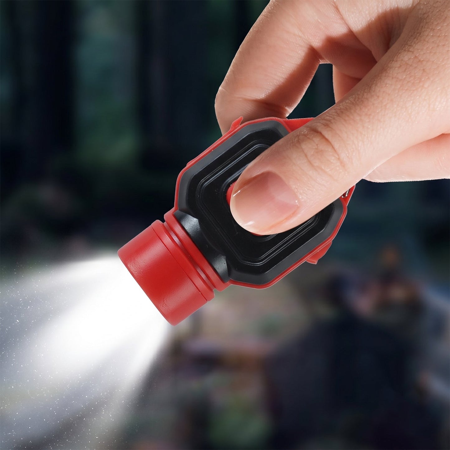 A hand holding the red and black mini LED flashlight, with its front light shining brightly in a dark outdoor setting.