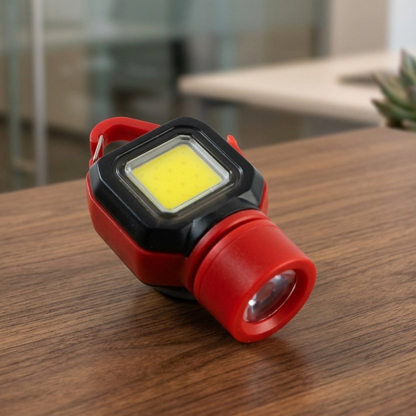 A red and black mini LED flashlight with a carabiner clip resting on a wooden table.