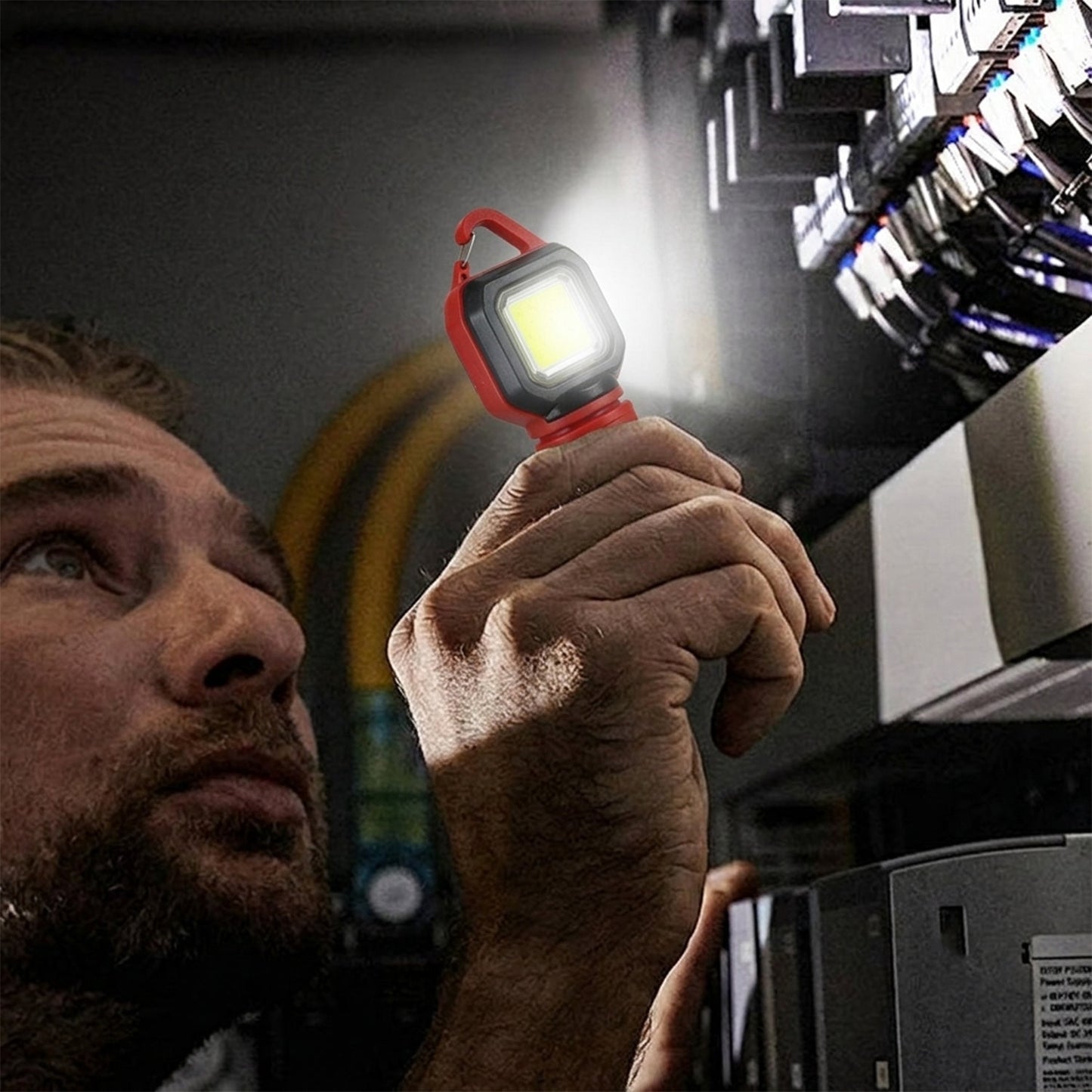 A man holding the red and black mini LED flashlight, using its side light to illuminate an electrical panel.