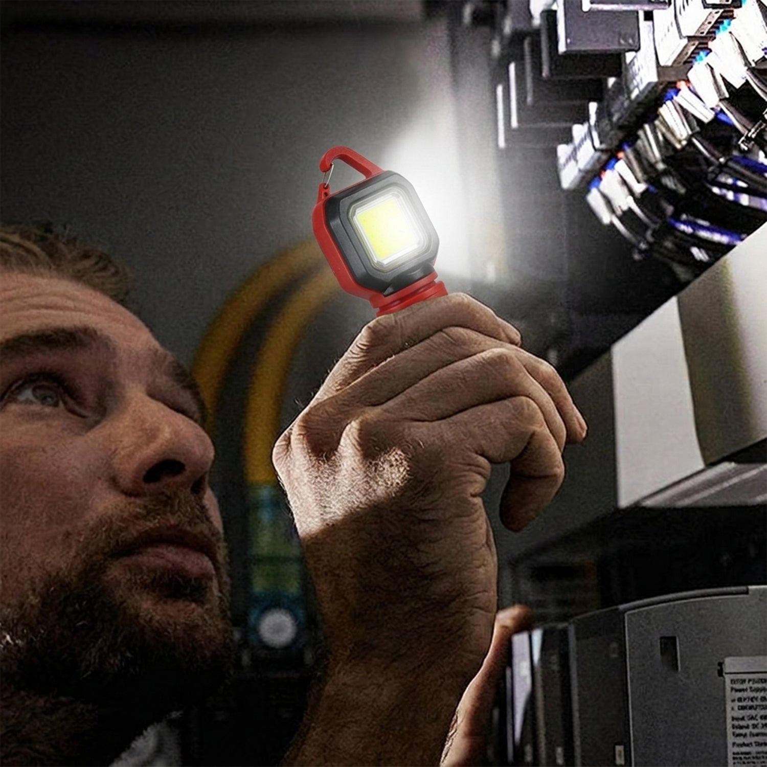 A man holding the red and black mini LED flashlight, using its side light to illuminate an electrical panel.