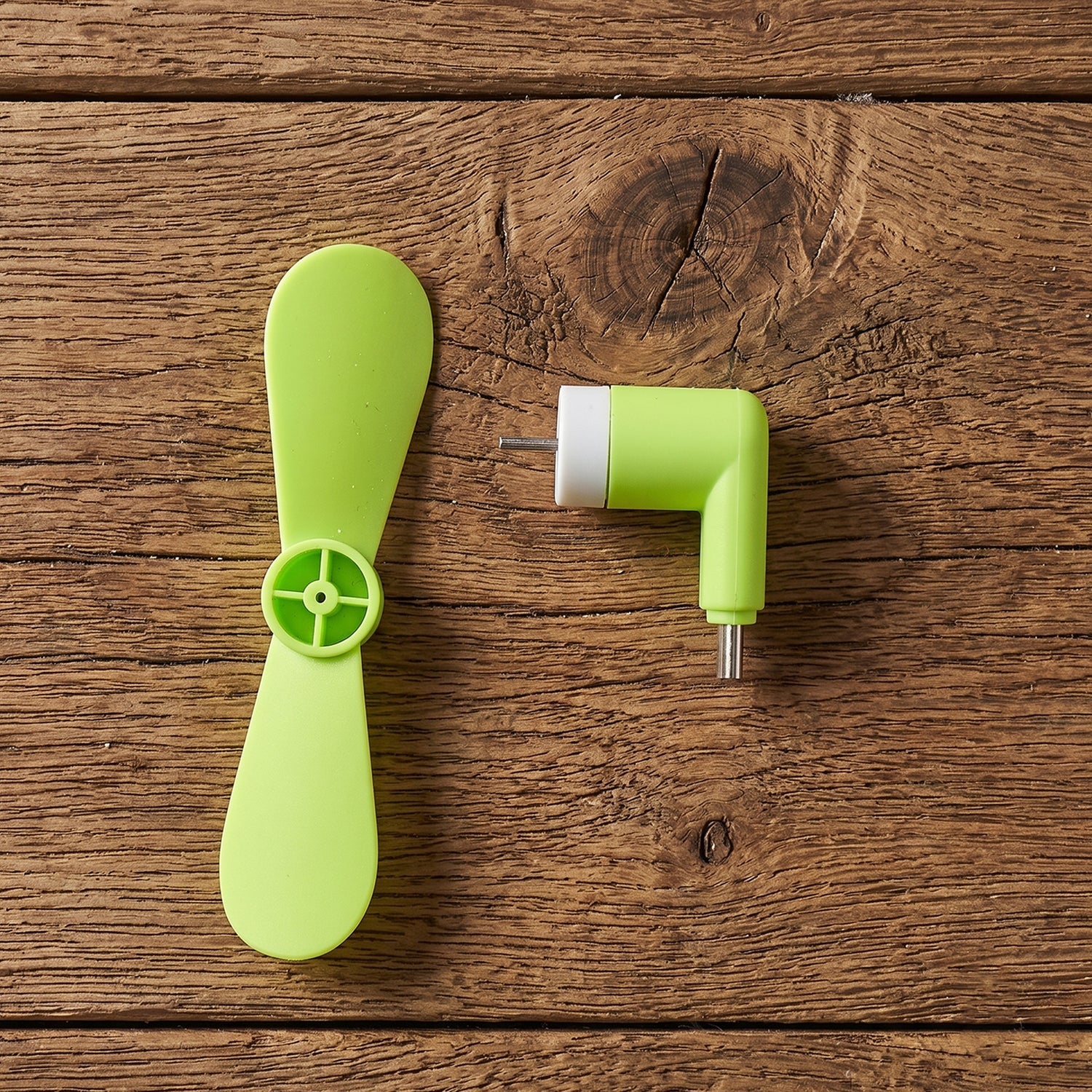 The bright green USB-C fan is disassembled into its two parts on a rustic wooden surface.
