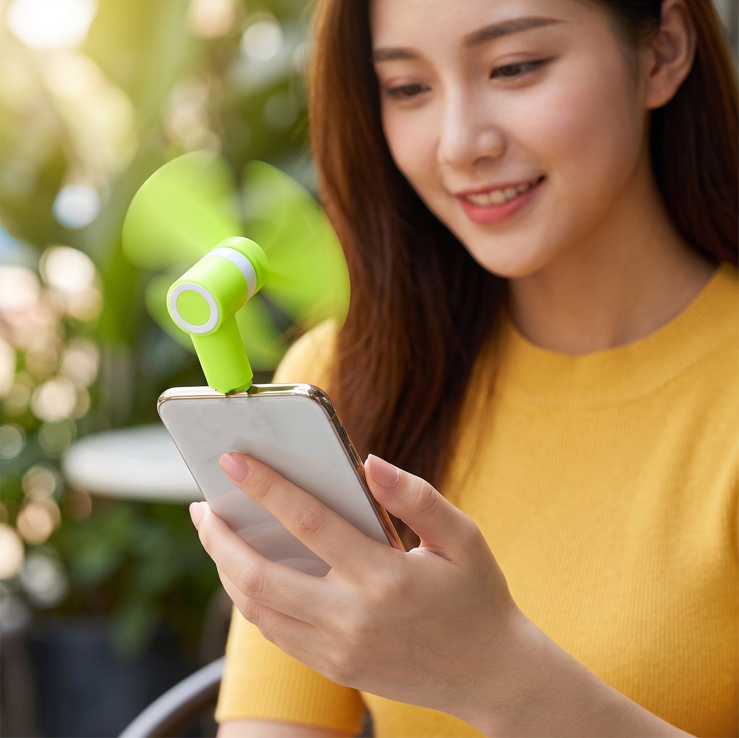 A woman smiles while holding a phone with a bright green USB-C fan plugged in.