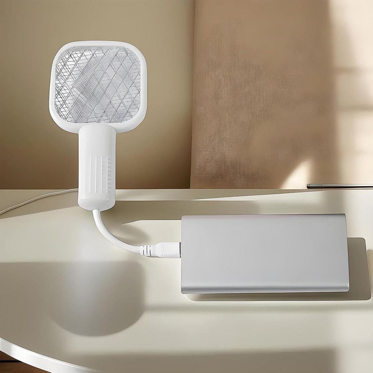 A white electric bug zapper with a square head and ribbed handle, connected to a USB cable, plugged into a silver power bank
