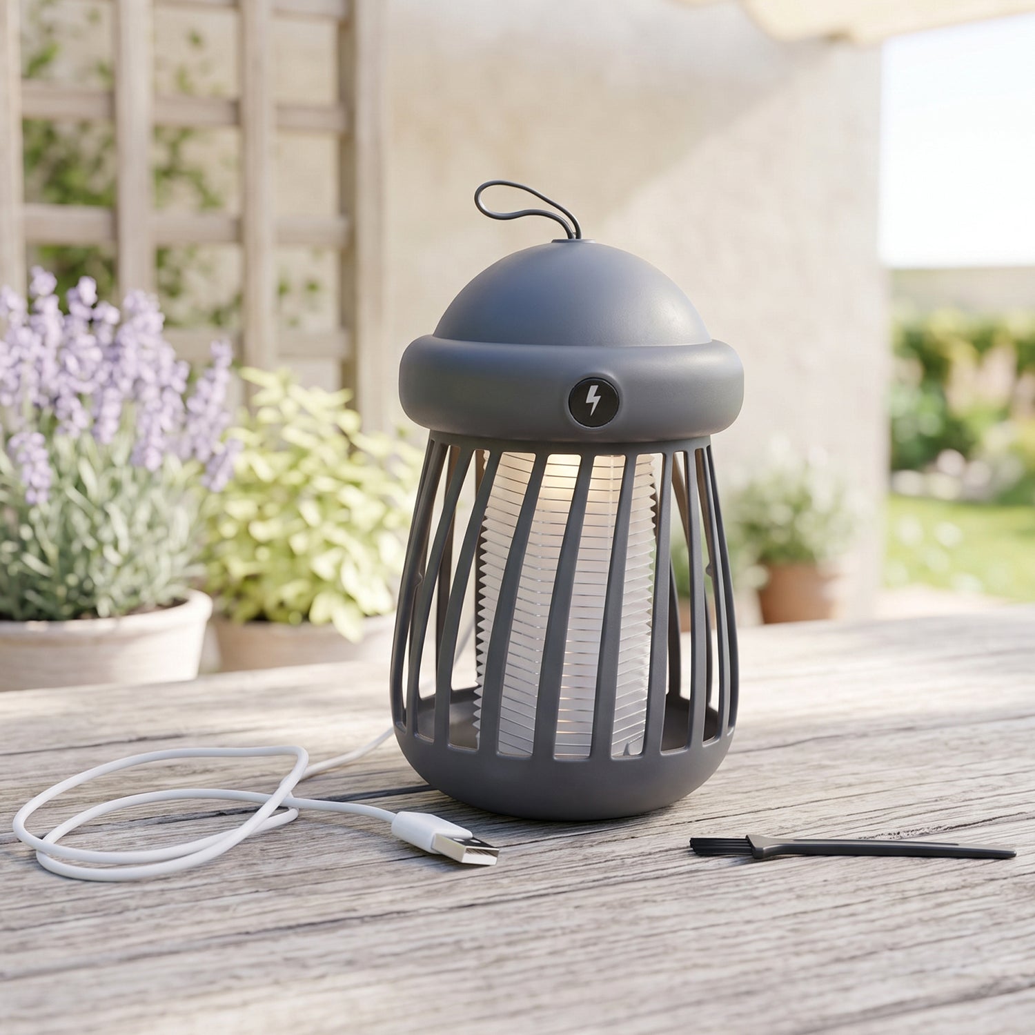 A gray mosquito killer lamp with a white light and a white USB cable sits on a wooden outdoor table with potted plants in
