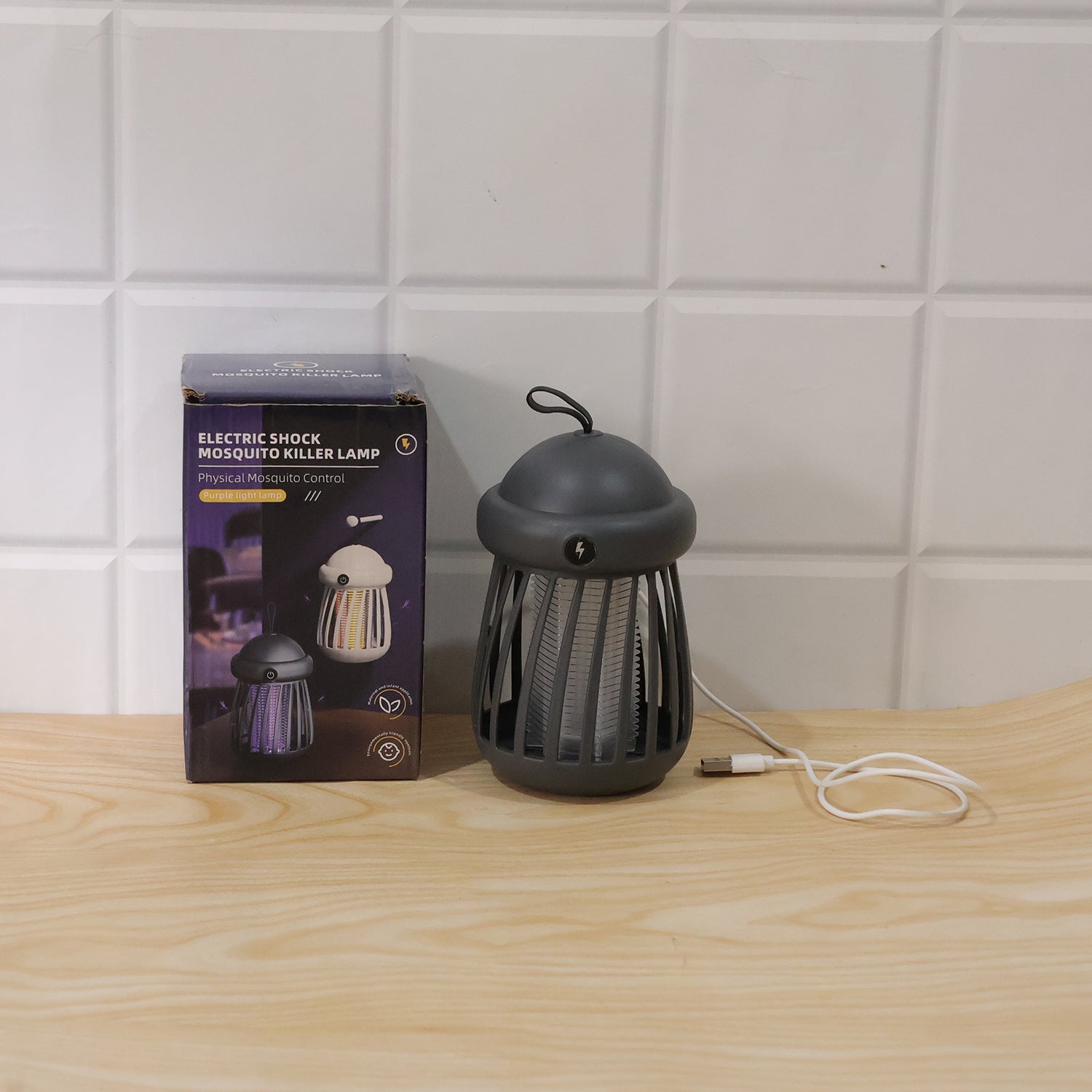 A gray mosquito killer lamp with a white light, a white USB cable, and its product box are displayed on a light wooden