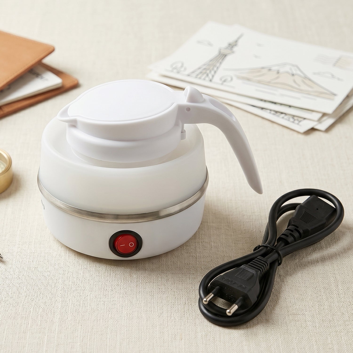 A white collapsible electric kettle, collapsed, with a red power button and a black power cord on a light-colored textured