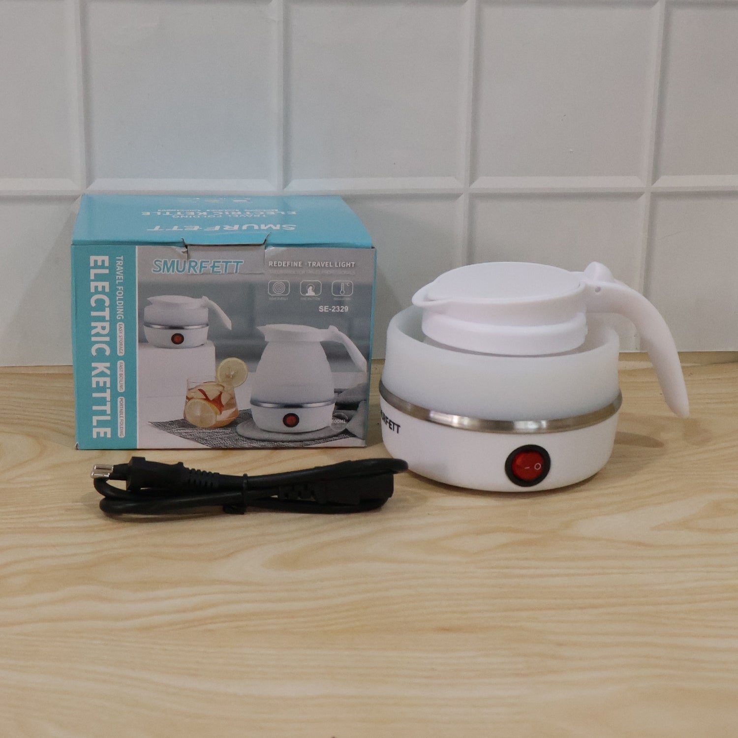 A white collapsible electric kettle, collapsed, with a red power button, a black power cord, and its blue and white product