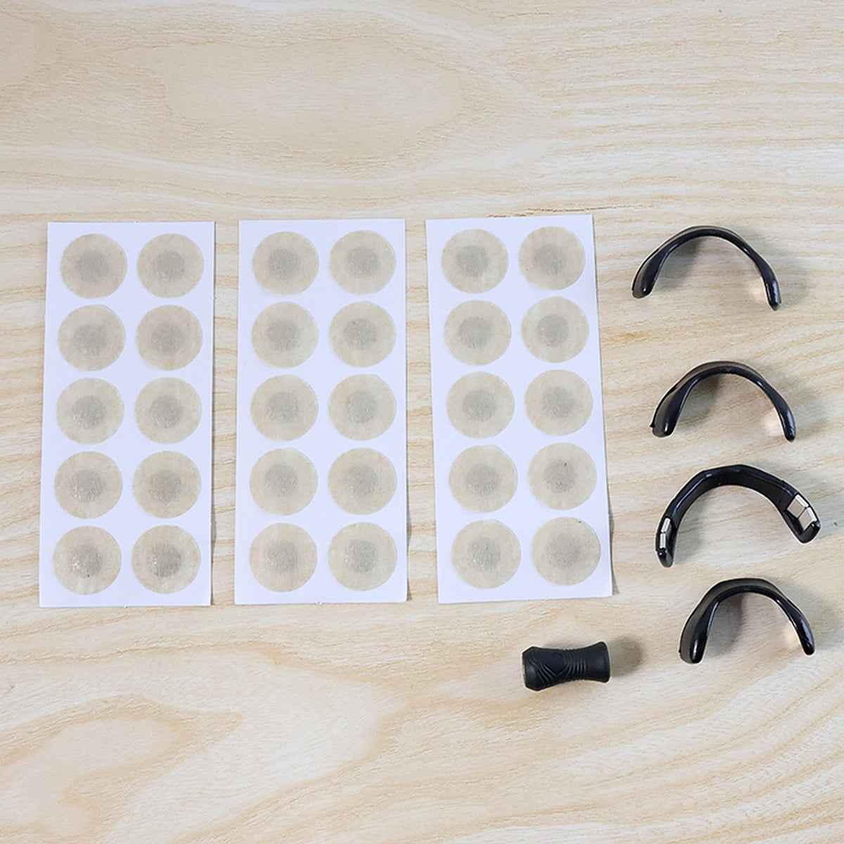 Three sheets of beige circular patches and four black nasal dilators with an applicator on a wooden surface.