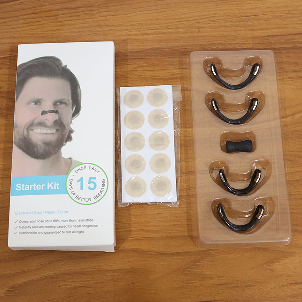 White box for nasal dilator starter kit, a small bag of beige circular patches, and a clear tray with four black nasal