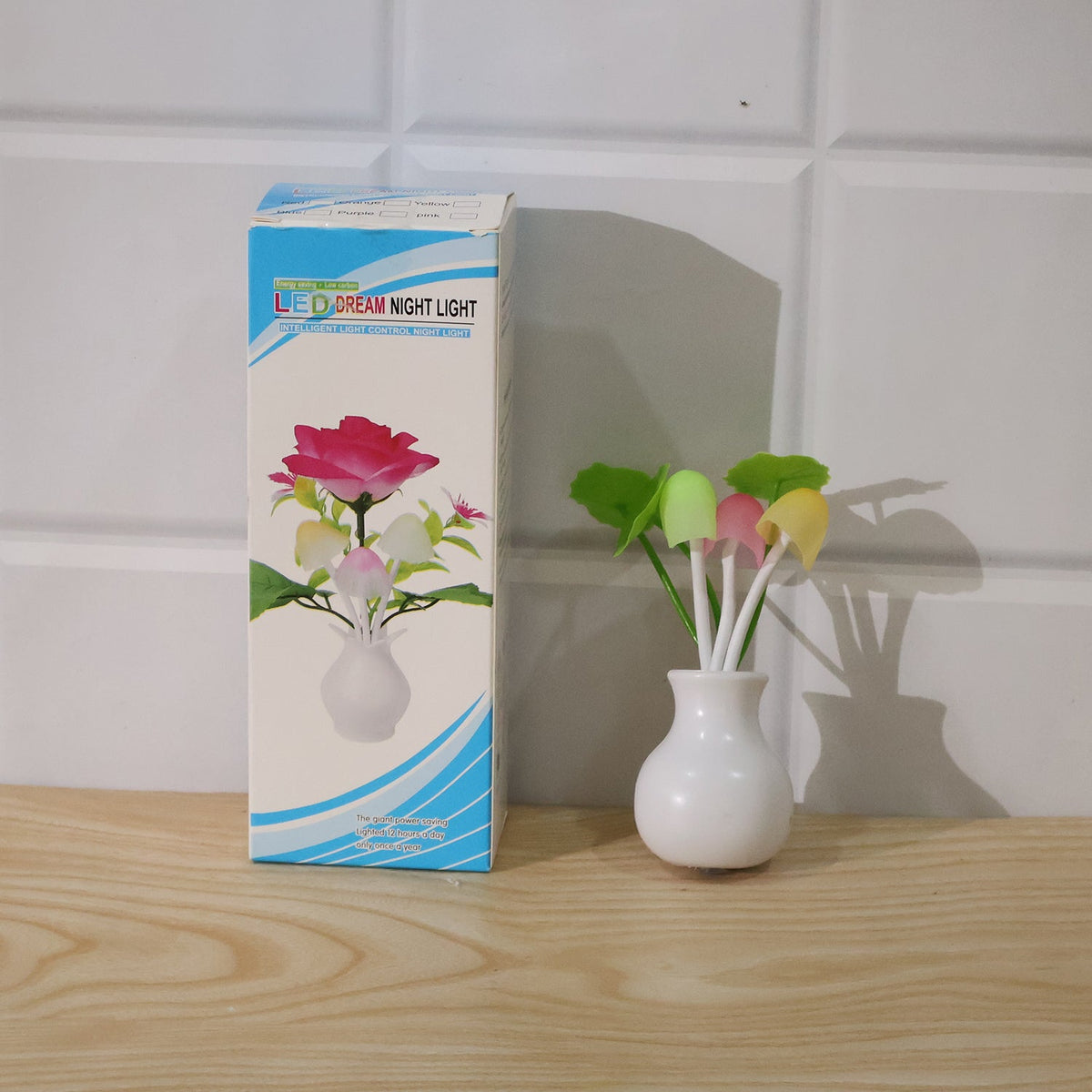 The white vase-shaped night light with colorful mushroom-like lights sits next to its product box, which features a rose
