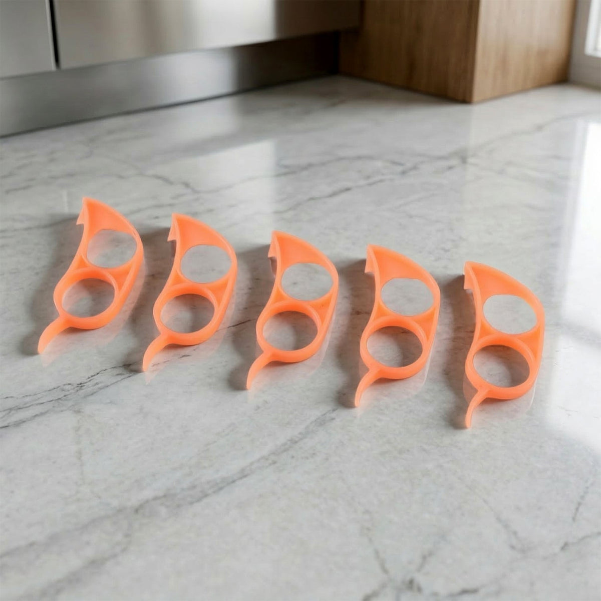 Five orange plastic citrus peelers are neatly lined up on a speckled gray and white countertop.