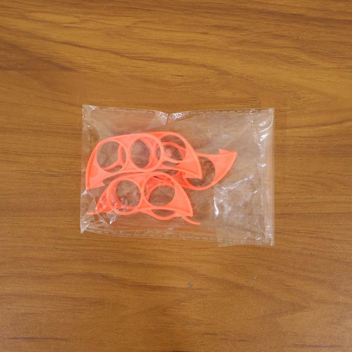 Four orange plastic citrus peelers are visible inside a clear plastic bag on a wooden surface.