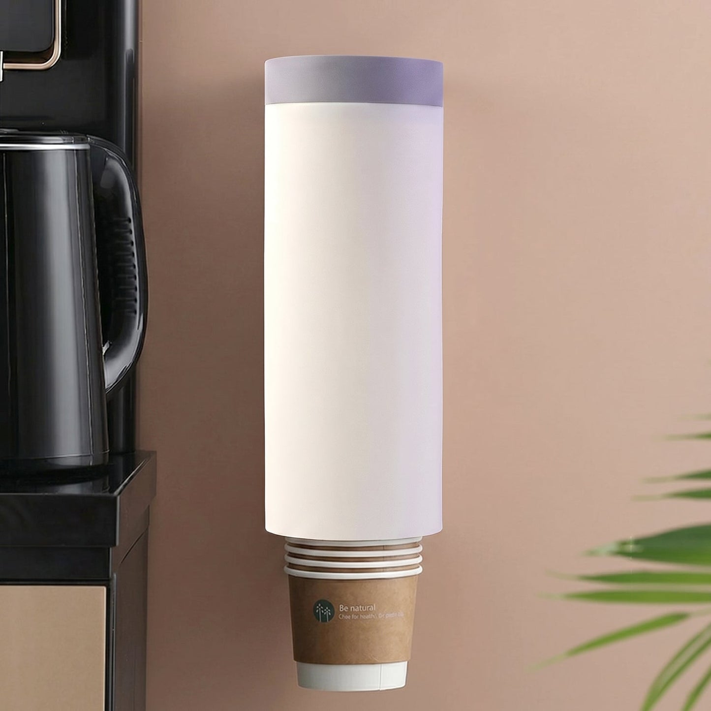 A white wall-mounted cup dispenser with a gray lid, holding a stack of brown paper cups, next to a black kettle.