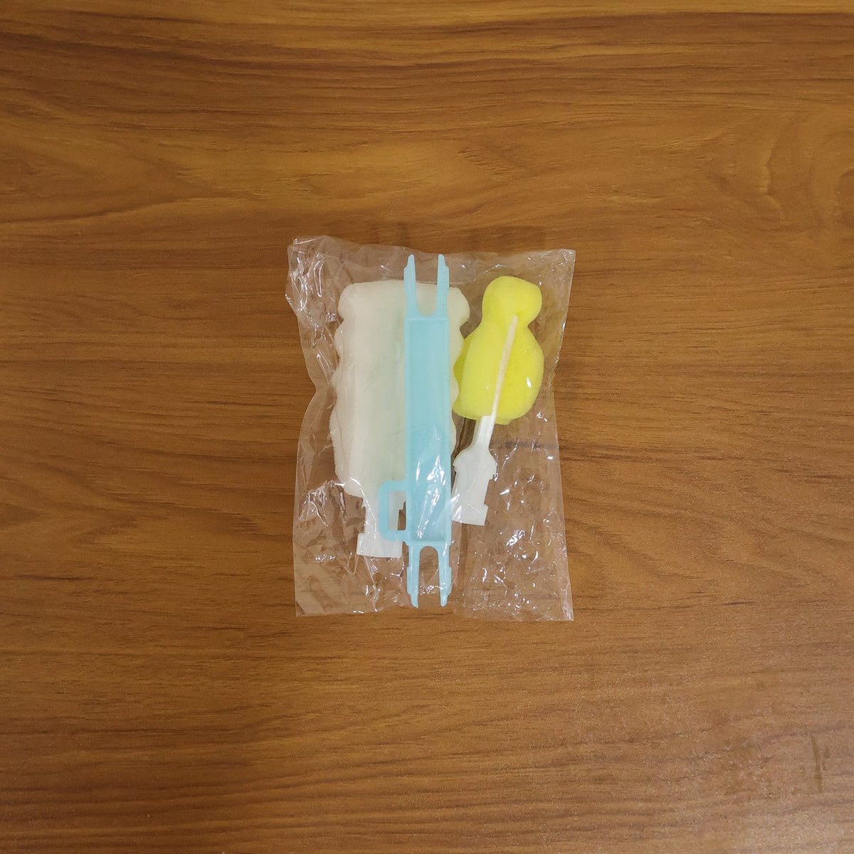 The disassembled cleaning brush components, including a handle and two sponge heads, packaged in a clear plastic bag on a