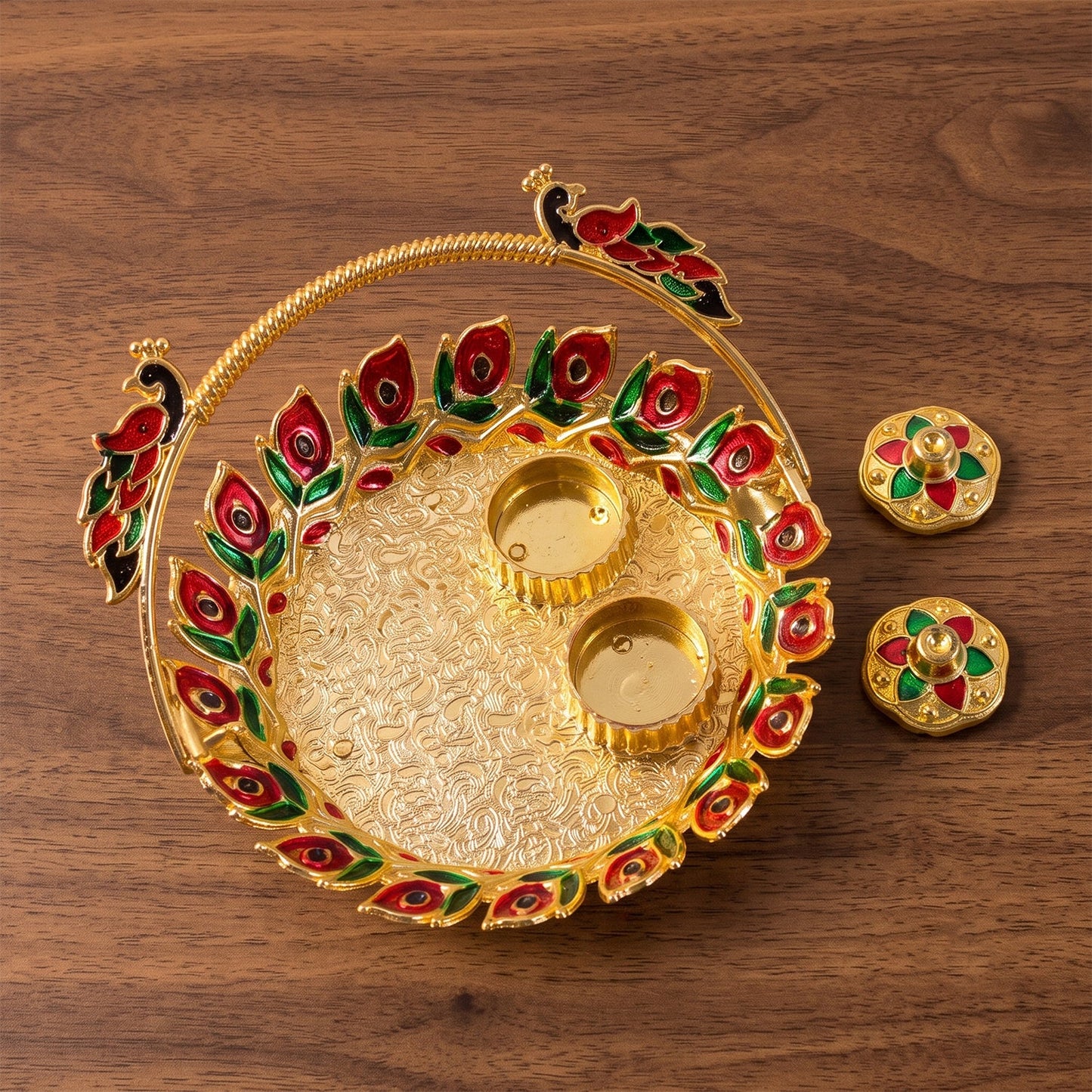 A golden kumkum dish with a peacock handle, with two empty golden cups and two lidded containers on a wooden surface.