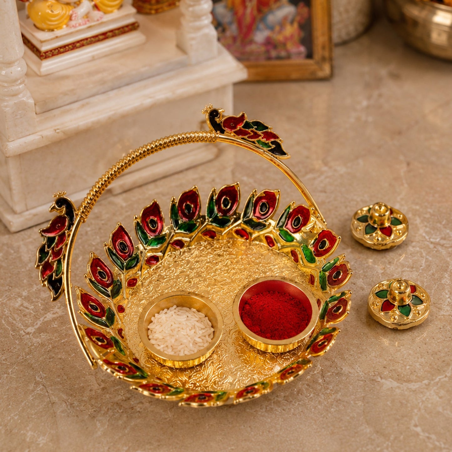 A golden kumkum dish with a peacock handle, holding red kumkum and white rice, with two lidded containers, on a textured
