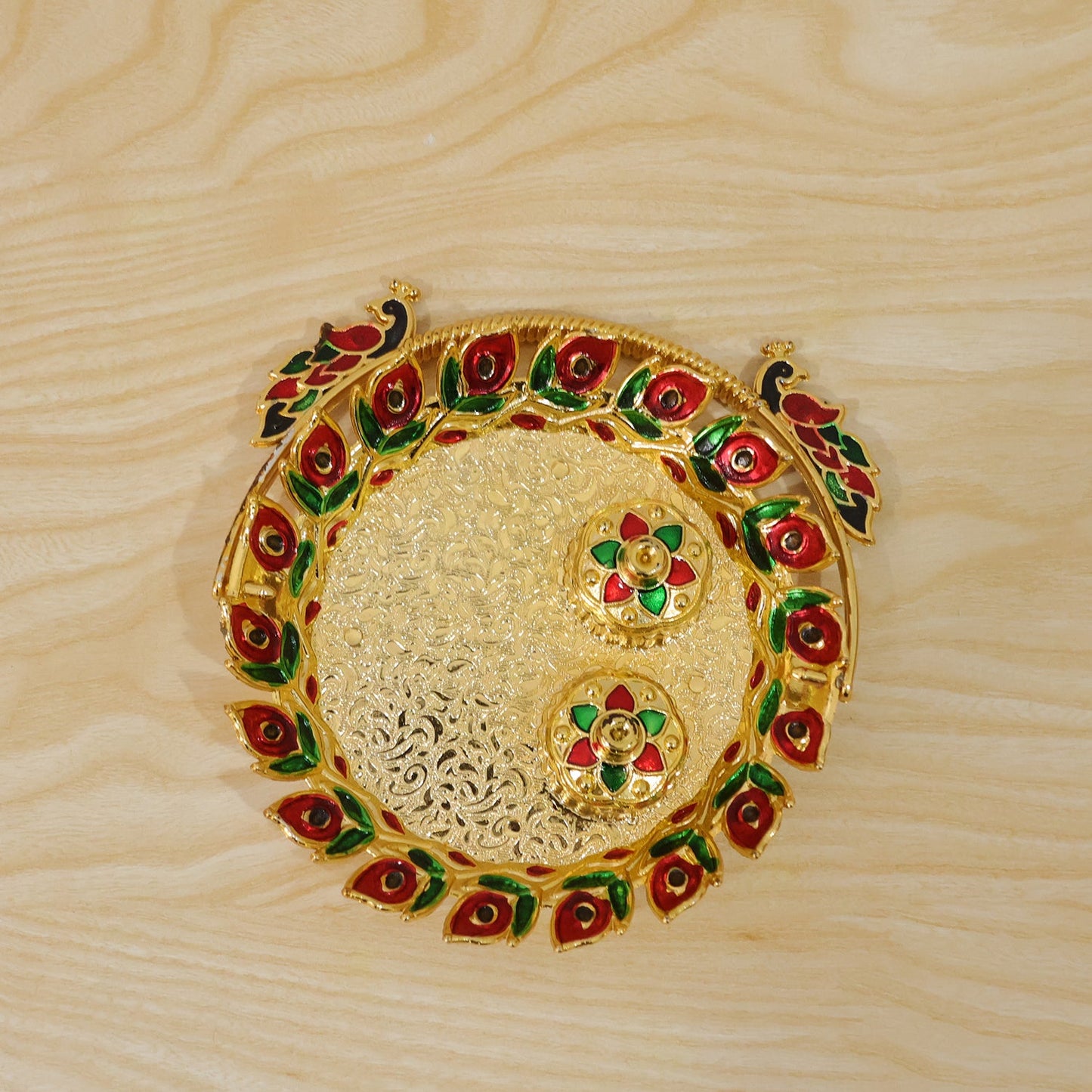 A top-down view of a golden kumkum dish with a peacock handle and two lidded containers on a light wooden surface.