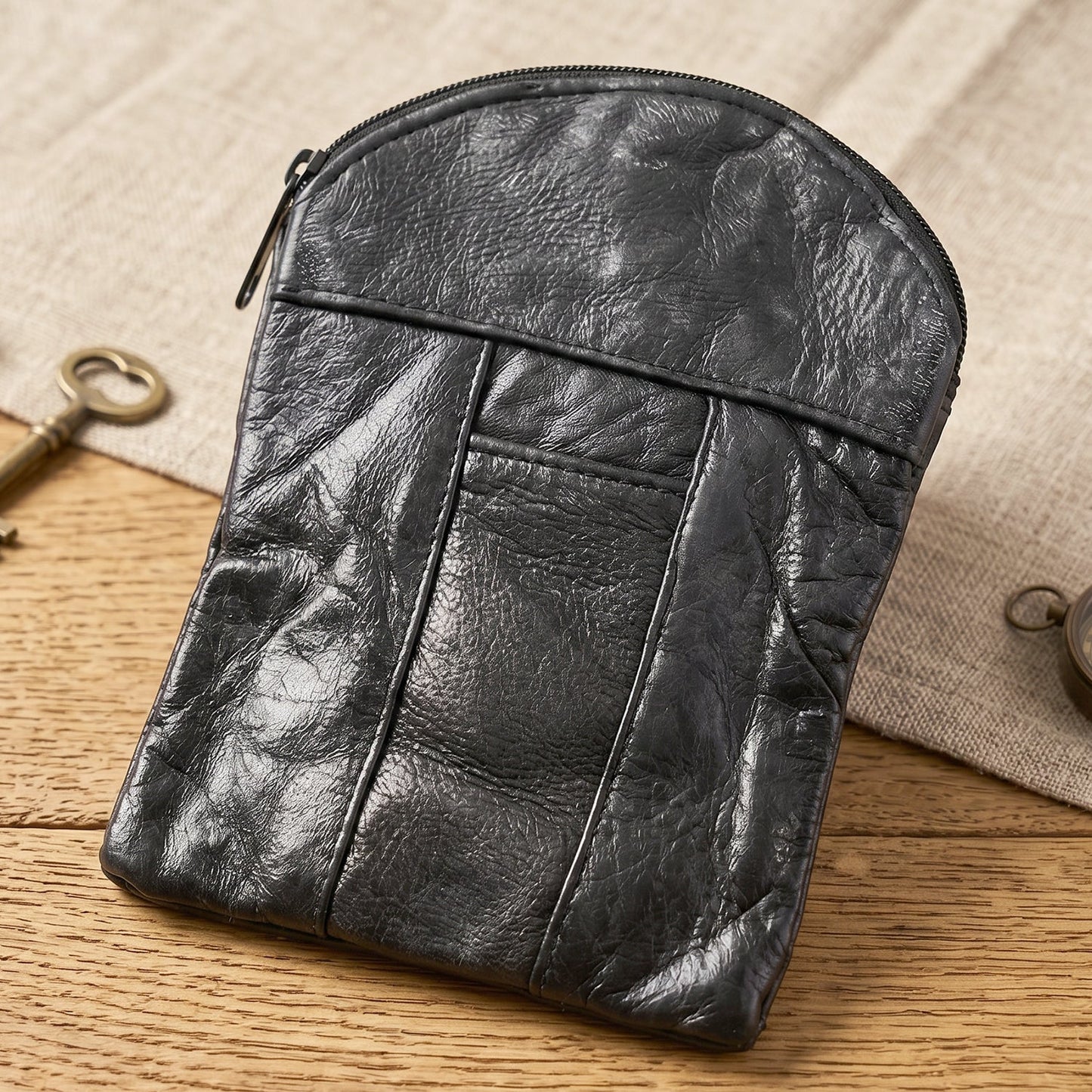 A black leather pouch with a textured surface and zipper, resting on a light fabric and wooden table.