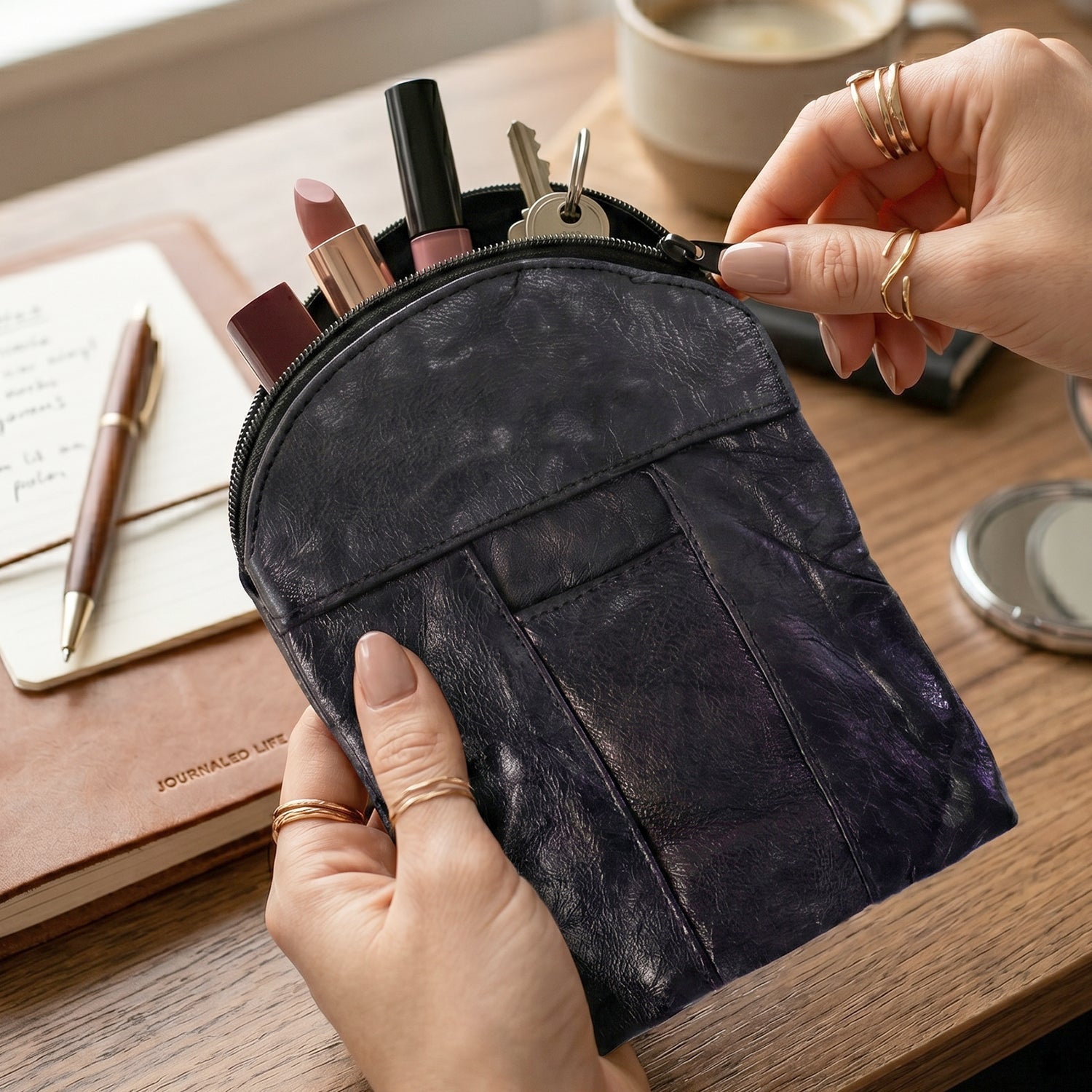 Hands holding an open black leather pouch filled with lipstick and keys on a wooden table.