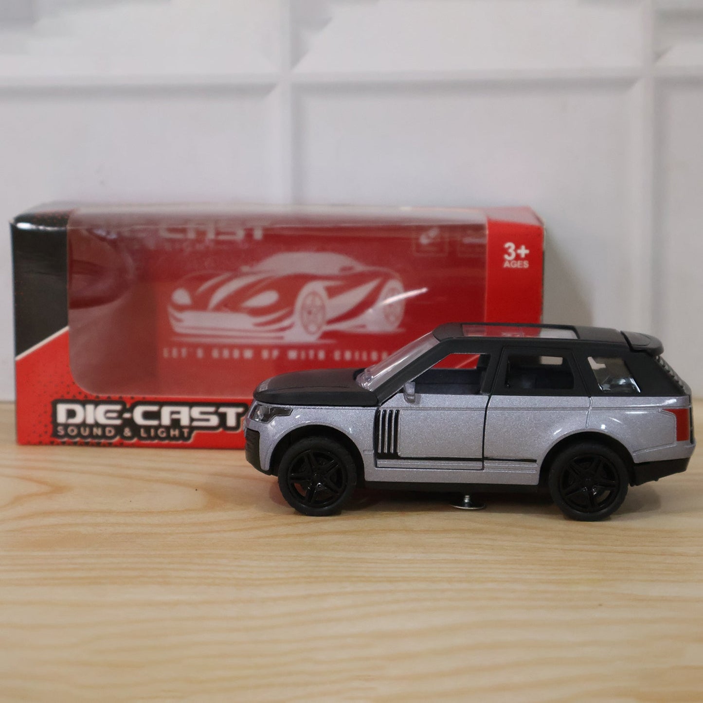 A silver and black die-cast toy SUV sits on a wooden surface next to its red and clear packaging box.